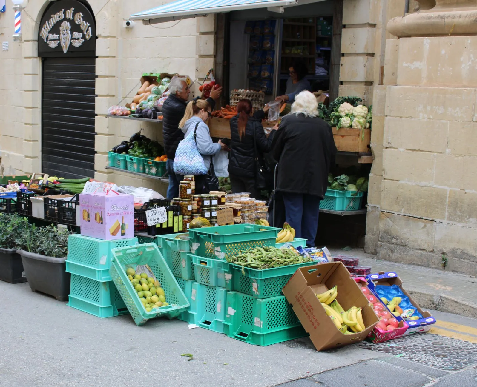 Busy street market with people buying fresh produce from outdoor stalls.